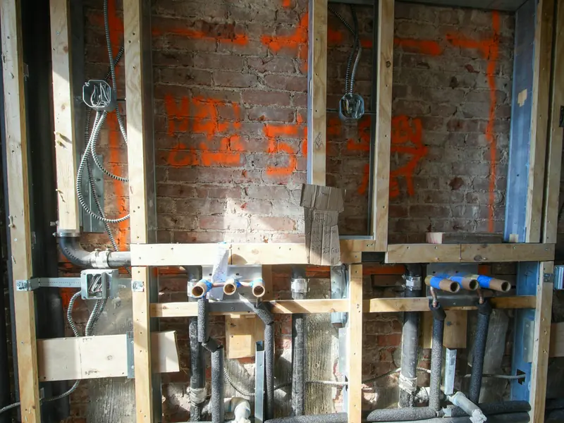 Supply and waste pipes roughed in behind an open bathroom wall before tiling