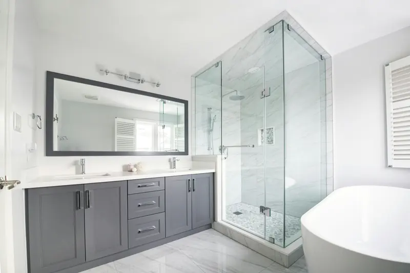 A renovated bathroom with a double vanity, a large mirror and a glass shower