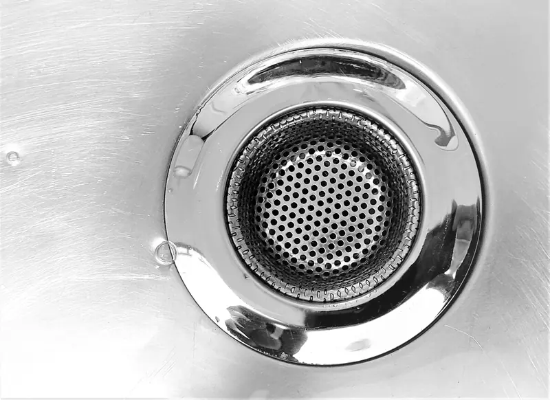 A stainless steel sink strainer over a kitchen drain