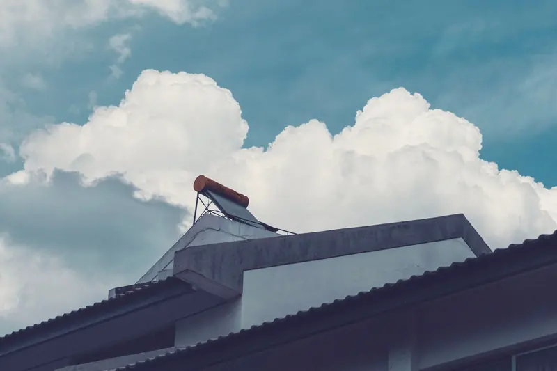A solar water heater mounted on the roof of a house under a cloudy summer sky