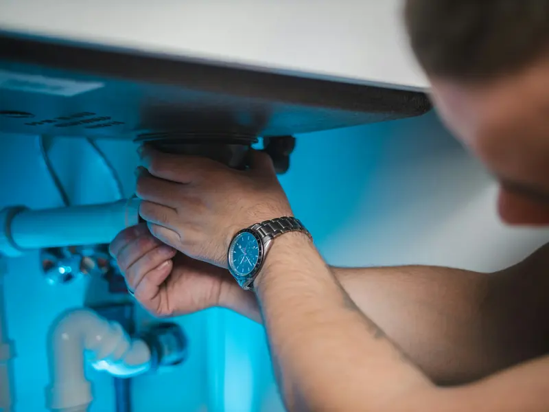 Hands working on a white waste pipe under a basin