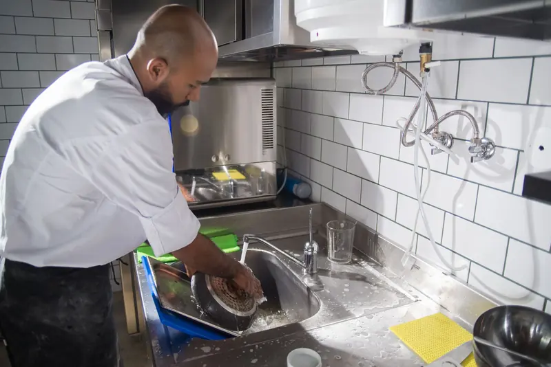 A chef rinsing dishes at a stainless steel sink in a commercial kitchen
