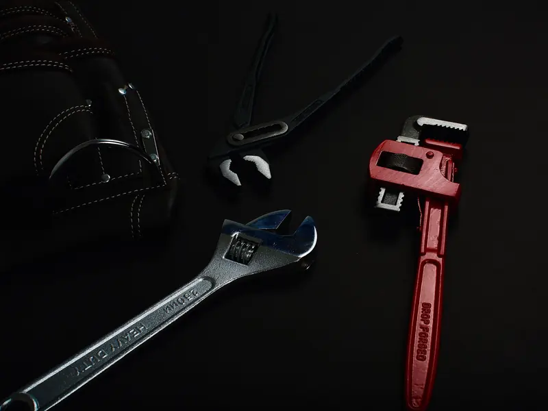 A pipe wrench and spanners laid out on a dark workbench