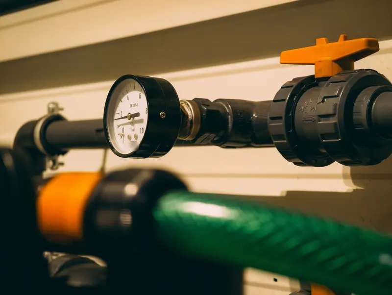 A pressure gauge fitted to a water pipe beside a valve