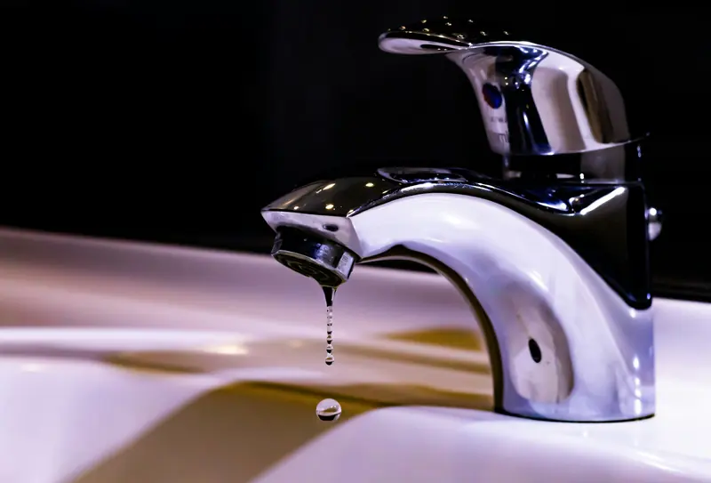 A chrome basin mixer with a drop of water at the spout