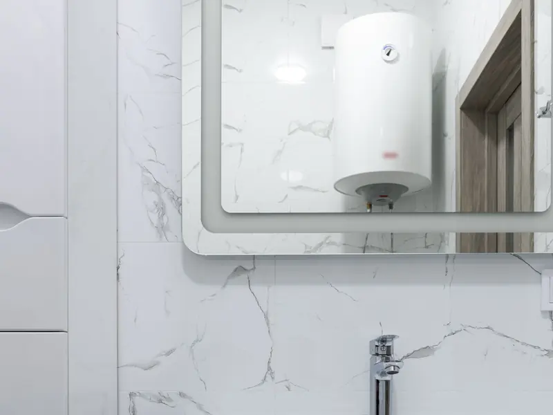 A wall-mounted electric water heater reflected in a bathroom mirror